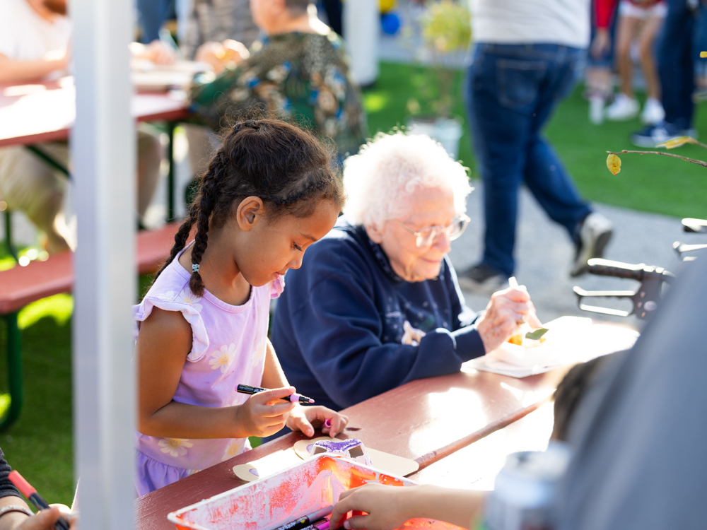 Young girl doing arts and crafts while sitting next to a senior at the Downtown Urbandale Block Party
